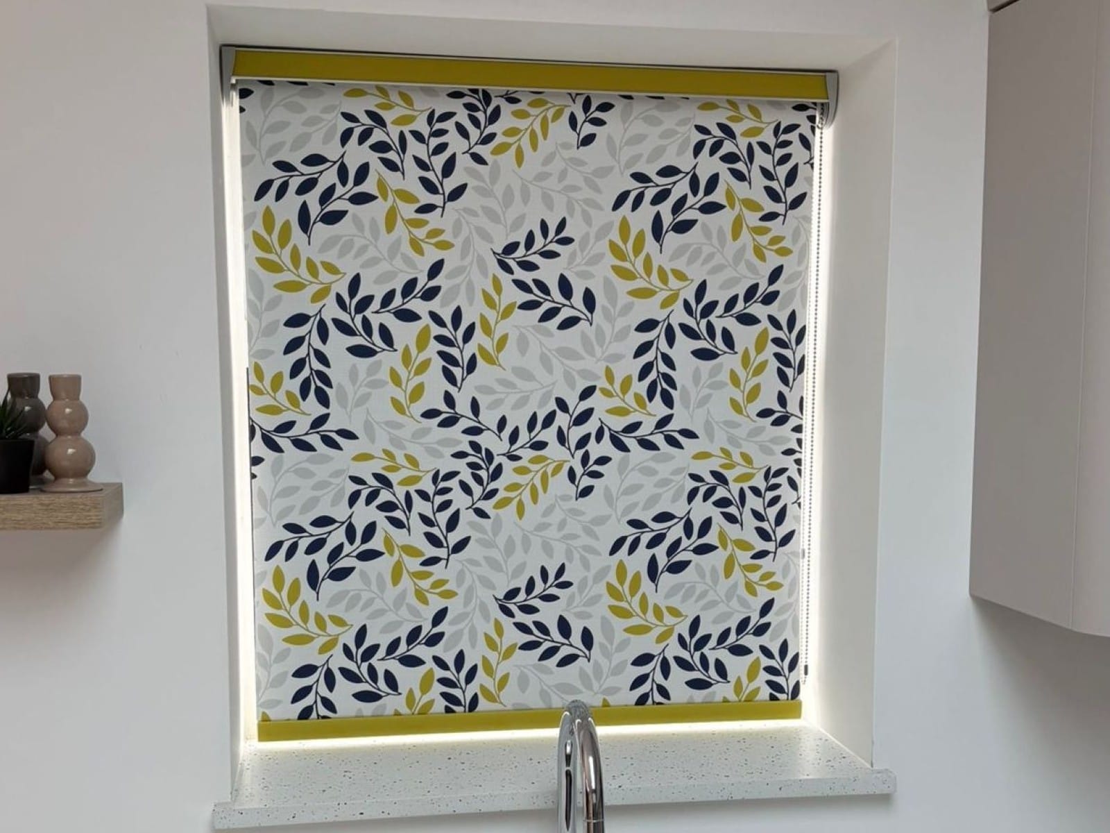 Made-to-measure Anycolour Roller Blind with a custom leaf pattern in yellow, navy, and grey, installed in a modern Essex kitchen.
