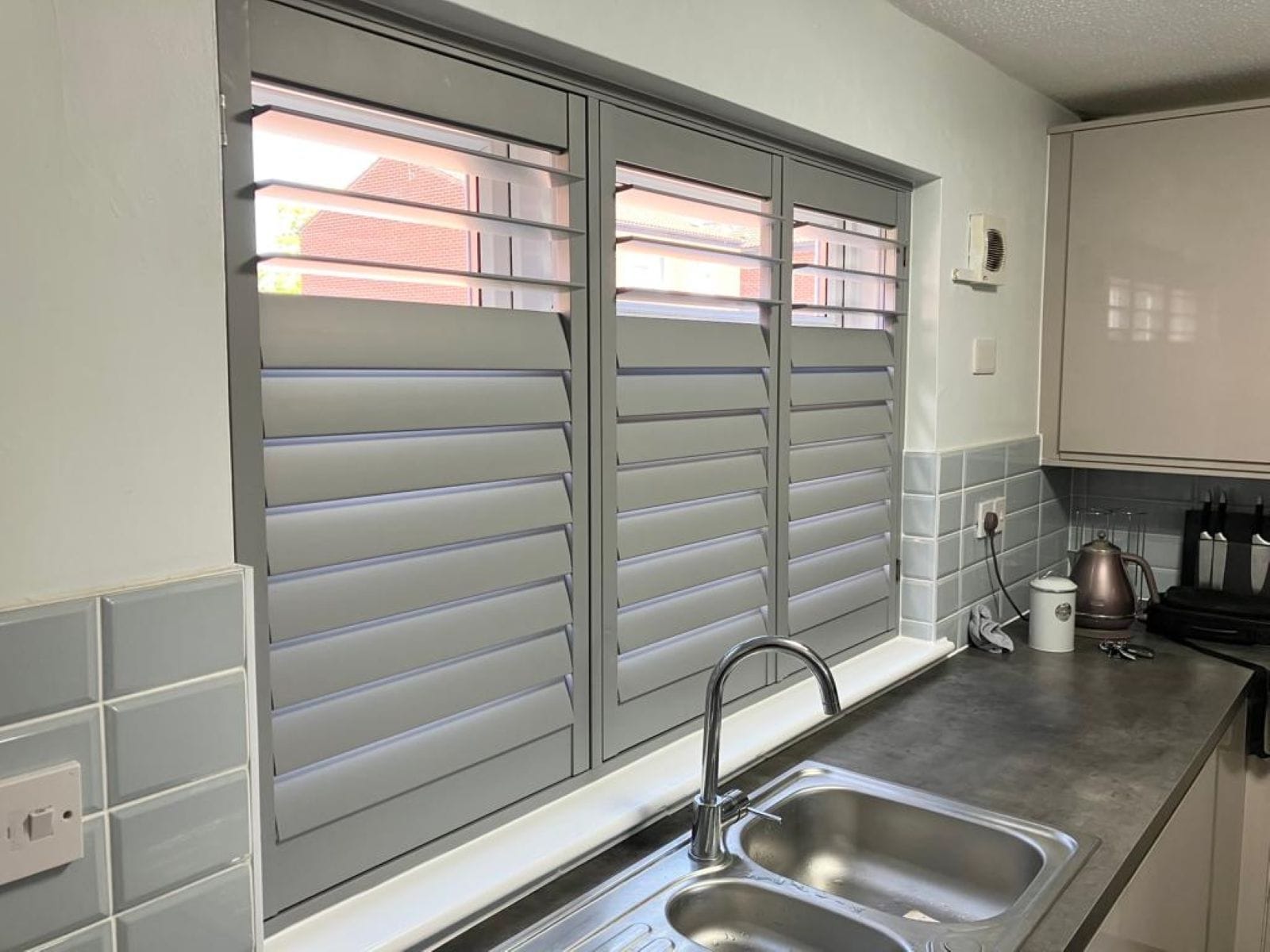 Signal grey plantation shutters installed in a modern Essex kitchen, offering privacy and light control.