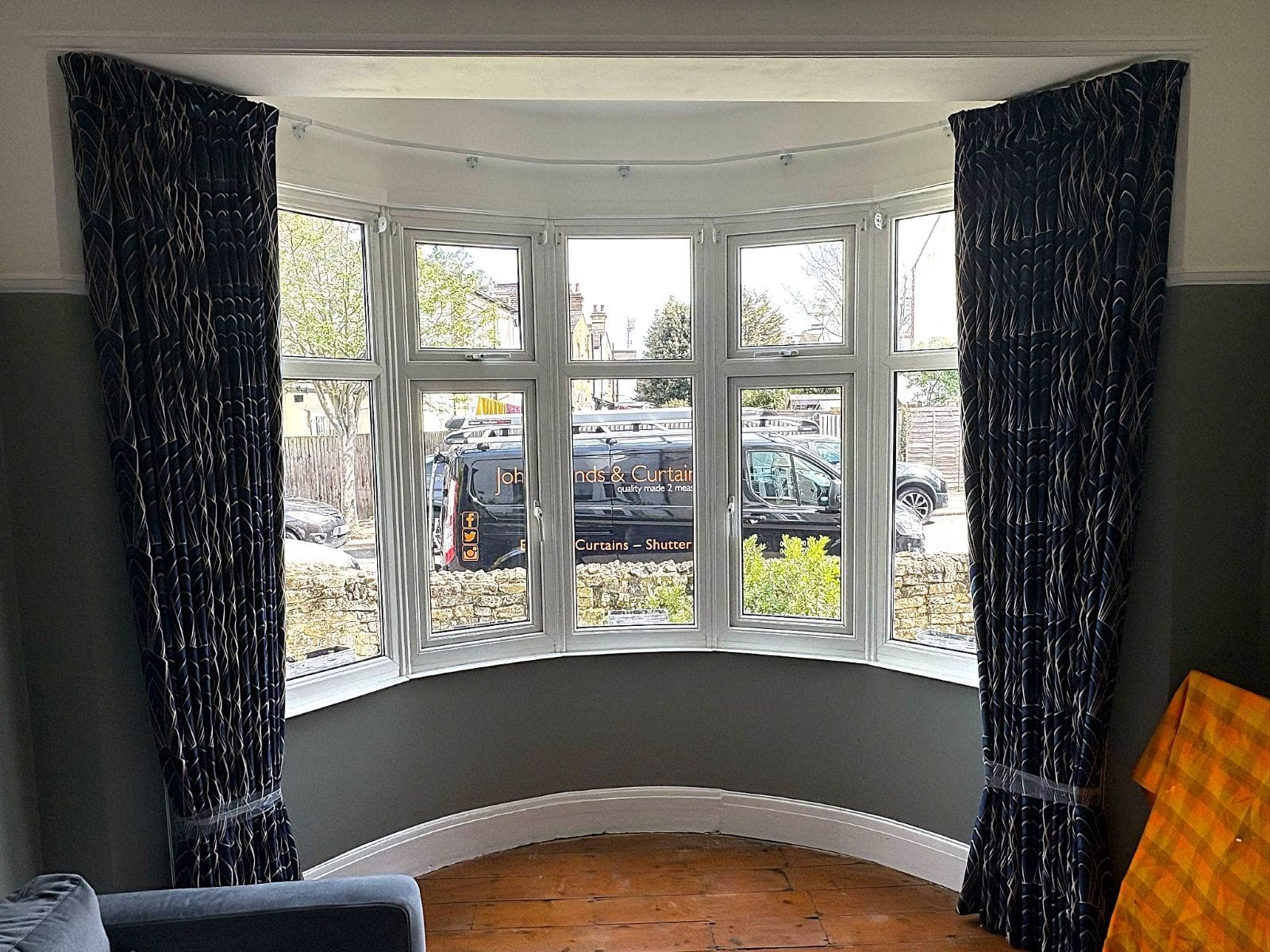 Pencil pleat curtains in navy patterned fabric, fitted to a curved bay window in an Essex home.