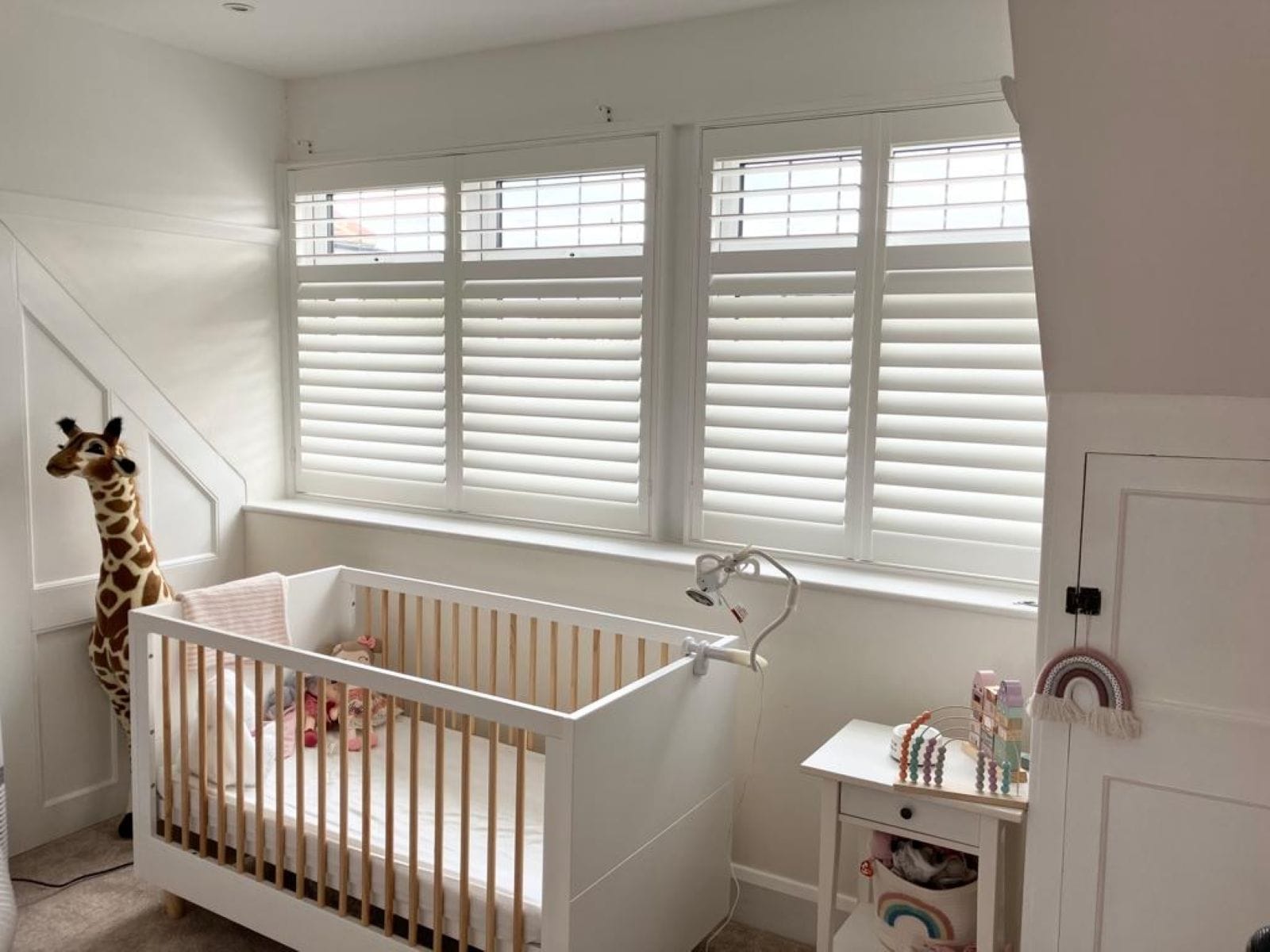 White plantation shutters fitted in a bright nursery, creating a calm and cosy space in an Essex home.