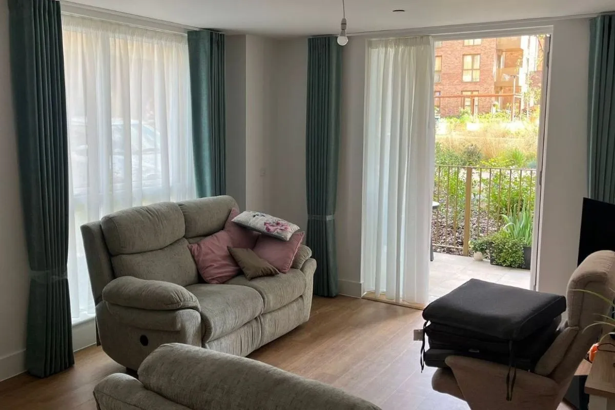 Turquoise wave curtains paired with white sheer curtains in a bright modern living room with patio doors and neutral furniture.