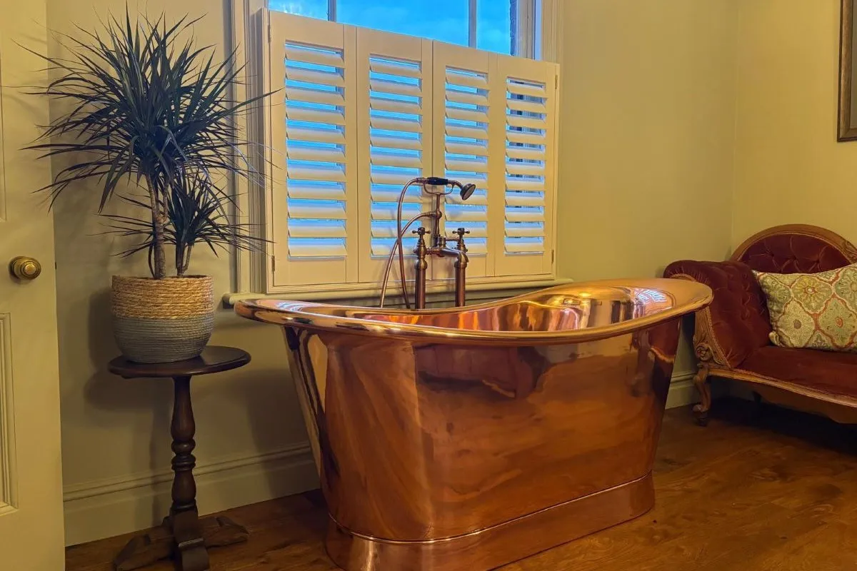 Café style moisture-resistant faux wood shutters installed above a freestanding bath, providing privacy and ventilation in a bathroom.