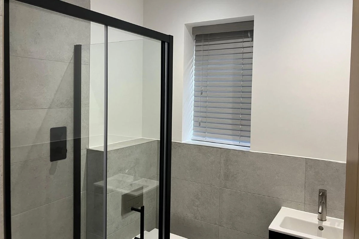 Grey faux wood Venetian blinds fitted to a bathroom window beside a shower, providing moisture-resistant privacy and adjustable light control.