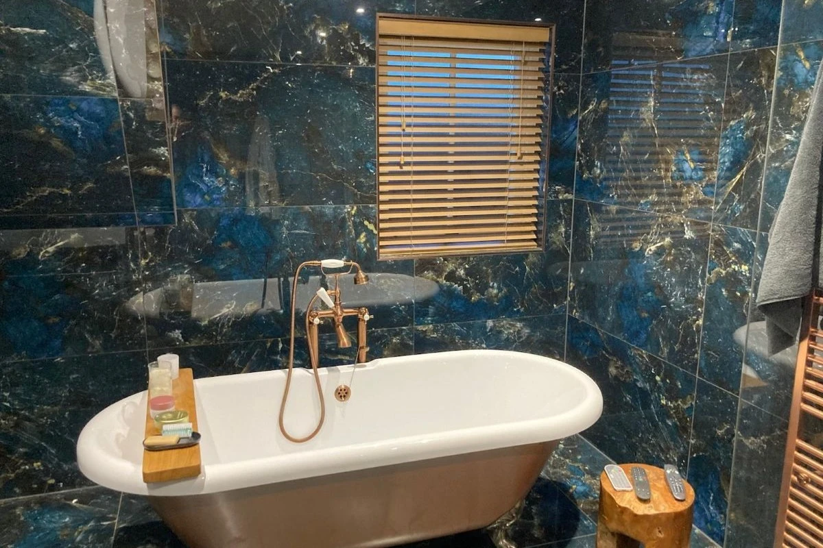 Faux wood Venetian blinds fitted to a bathroom window above a freestanding bath, providing moisture-resistant privacy and adjustable light control.