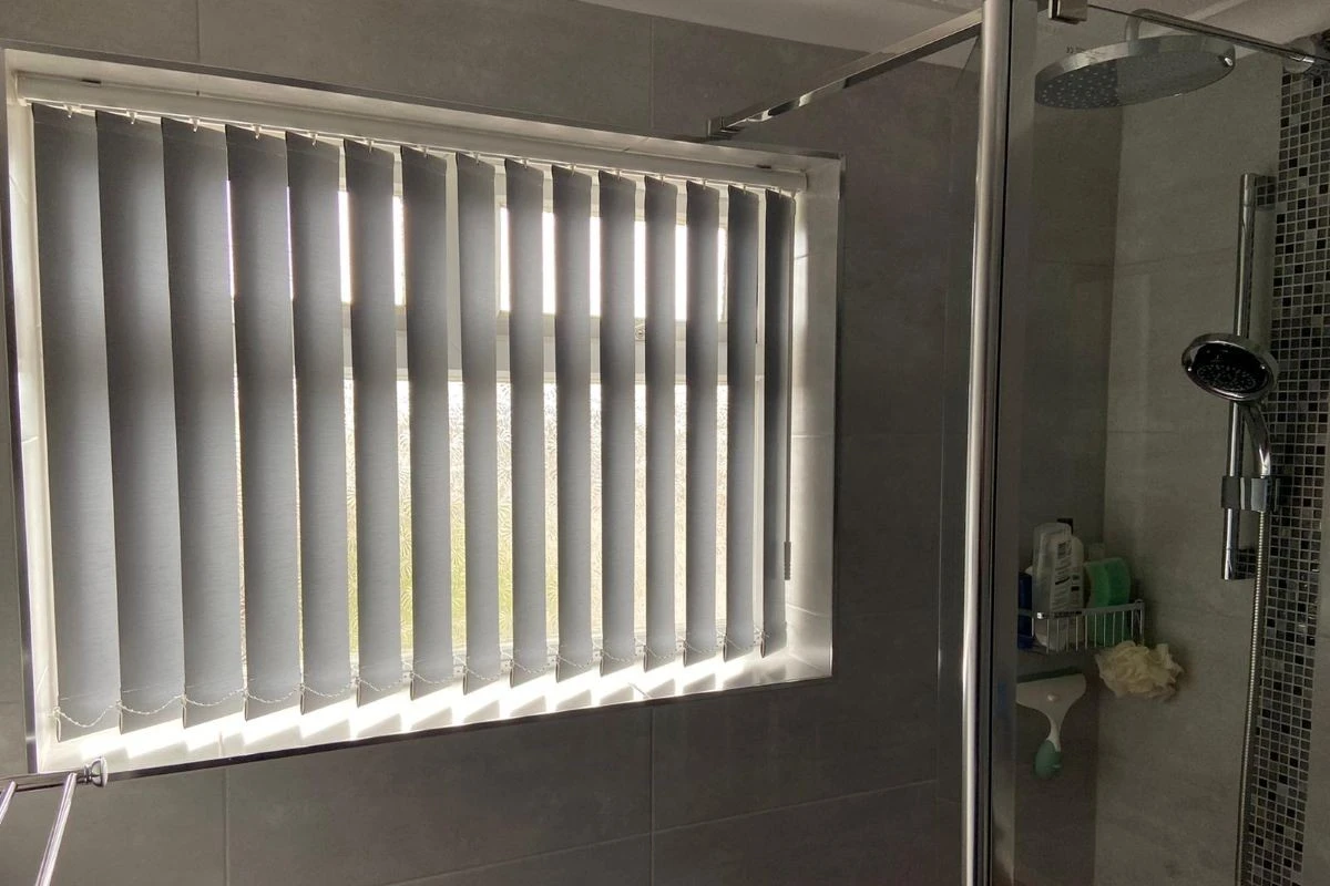 PVC vertical blinds fitted to a bathroom window beside a shower, providing waterproof privacy and adjustable light control.