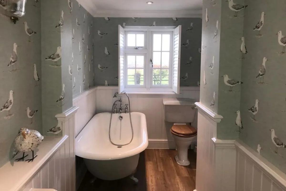 White bathroom shutters fitted to a window above a freestanding bath, providing privacy and light control in a traditional bathroom.