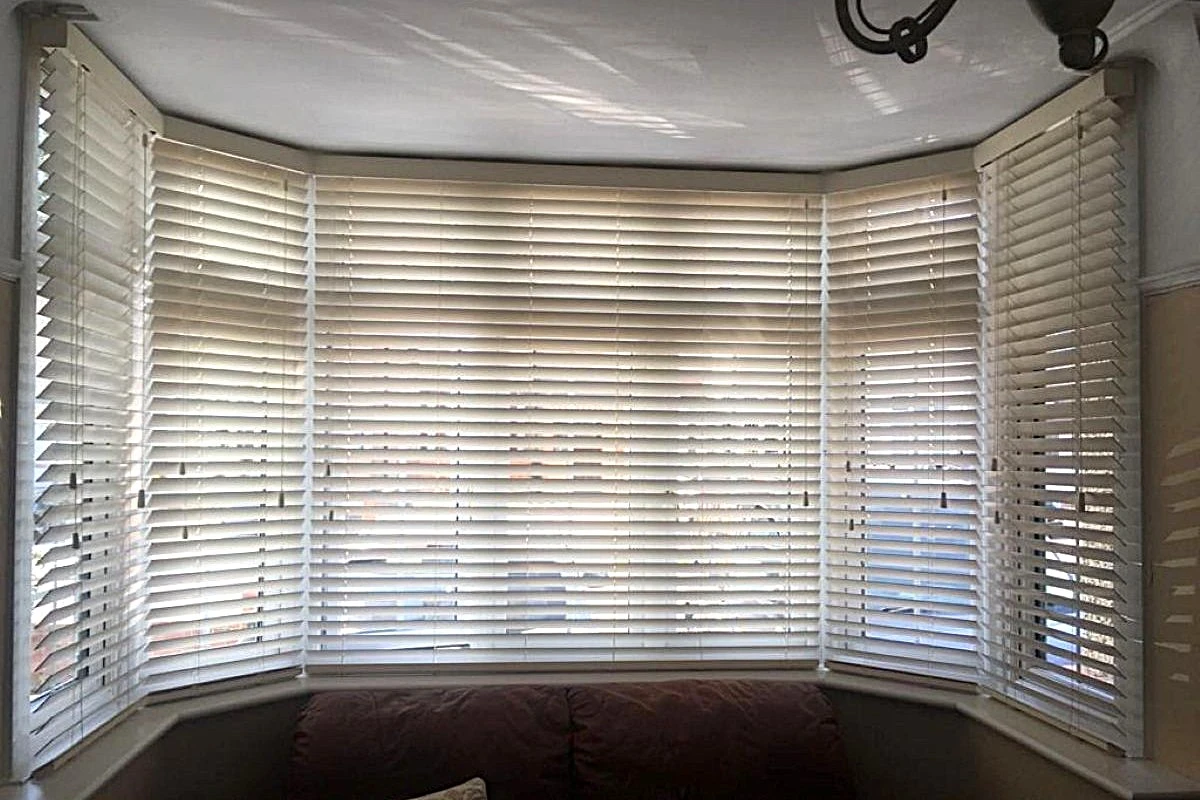 Cream 50mm PVC venetian blinds fitted across a large bay window in a living room.