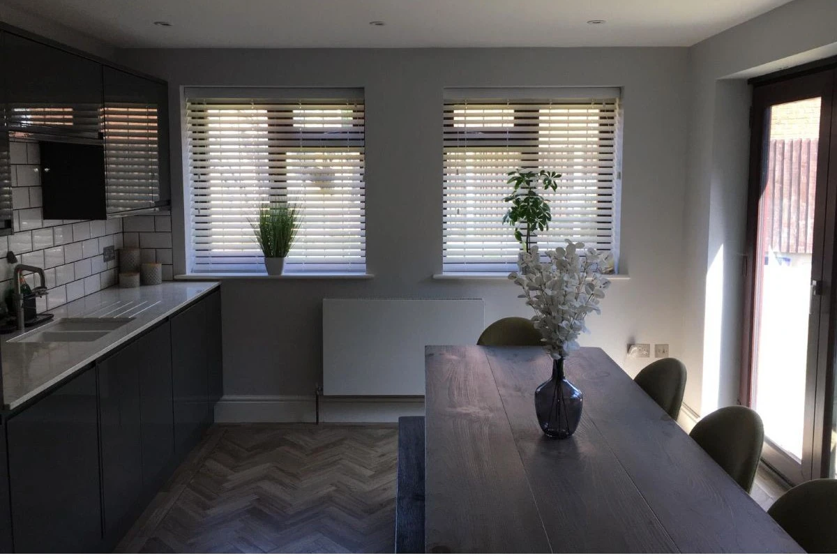 Faux Wood Venetian Blinds in a Modern Kitchen Faux Wood Venetian blinds fitted to multiple kitchen windows in a modern grey kitchen and dining area.
