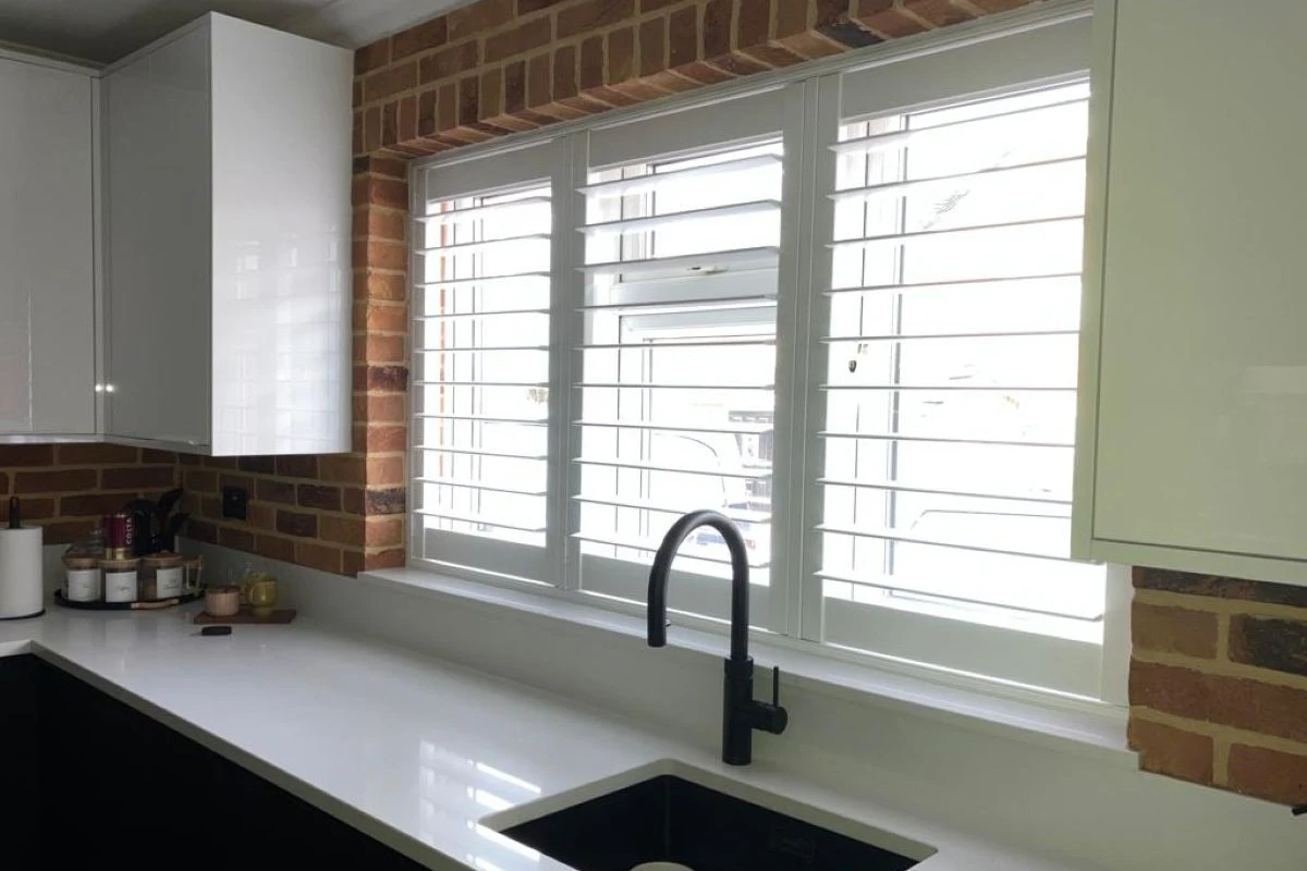 Faux Wood Shutters on Kitchen Sink Window with Brick Surround White faux wood plantation shutters fitted across a kitchen sink window with a brick feature wall
