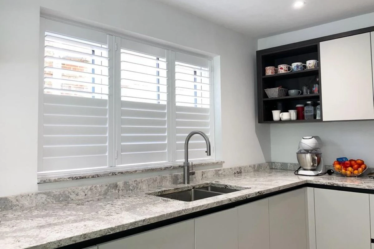 Faux Wood Shutters Above Kitchen Sink White faux wood plantation shutters fitted above a kitchen sink in a modern kitchen