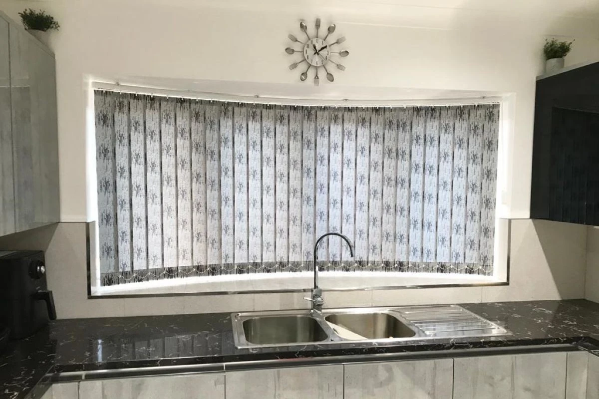 Curved vertical blinds fitted across a large kitchen sink window in a modern kitchen