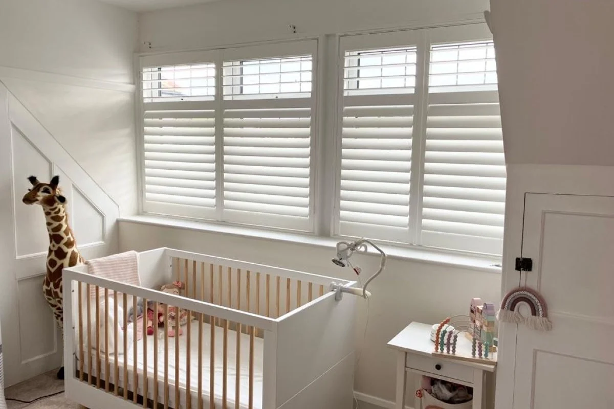 White Plantation Shutters in a Nursery Bedroom White plantation shutters with split-tilt louvres installed in a nursery bedroom, providing privacy, light control and a safe, cord-free window covering behind a baby cot.
