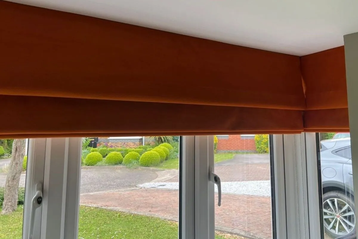Roman blind in Alvar Sunburst fabric, a rich orange shade, fitted neatly above a wide uPVC window.