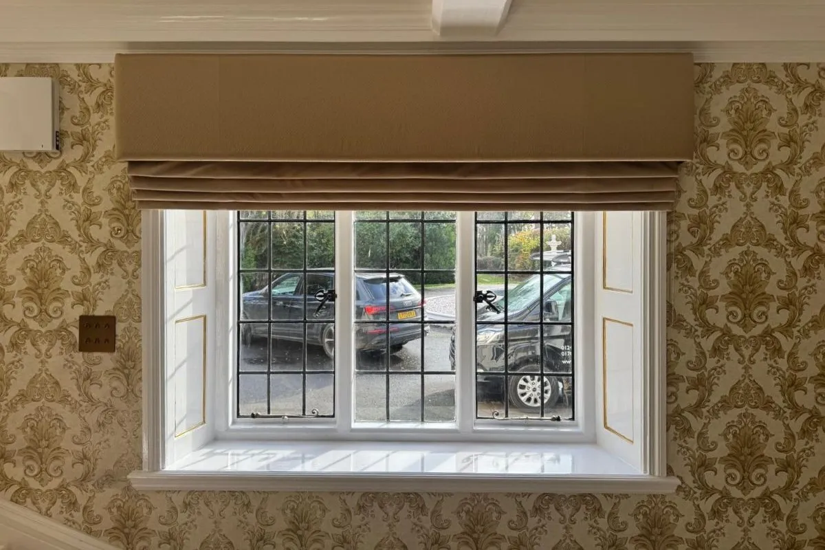 Traditional Roman blind with a matching beige pelmet fitted above a leaded window in a classic patterned interior.
