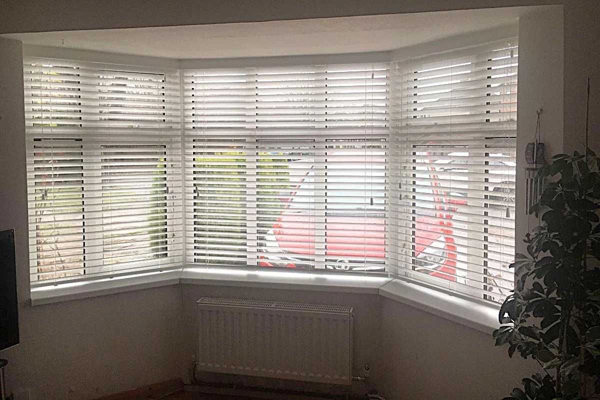 White faux wood venetian blinds installed in a bay window of a living room.