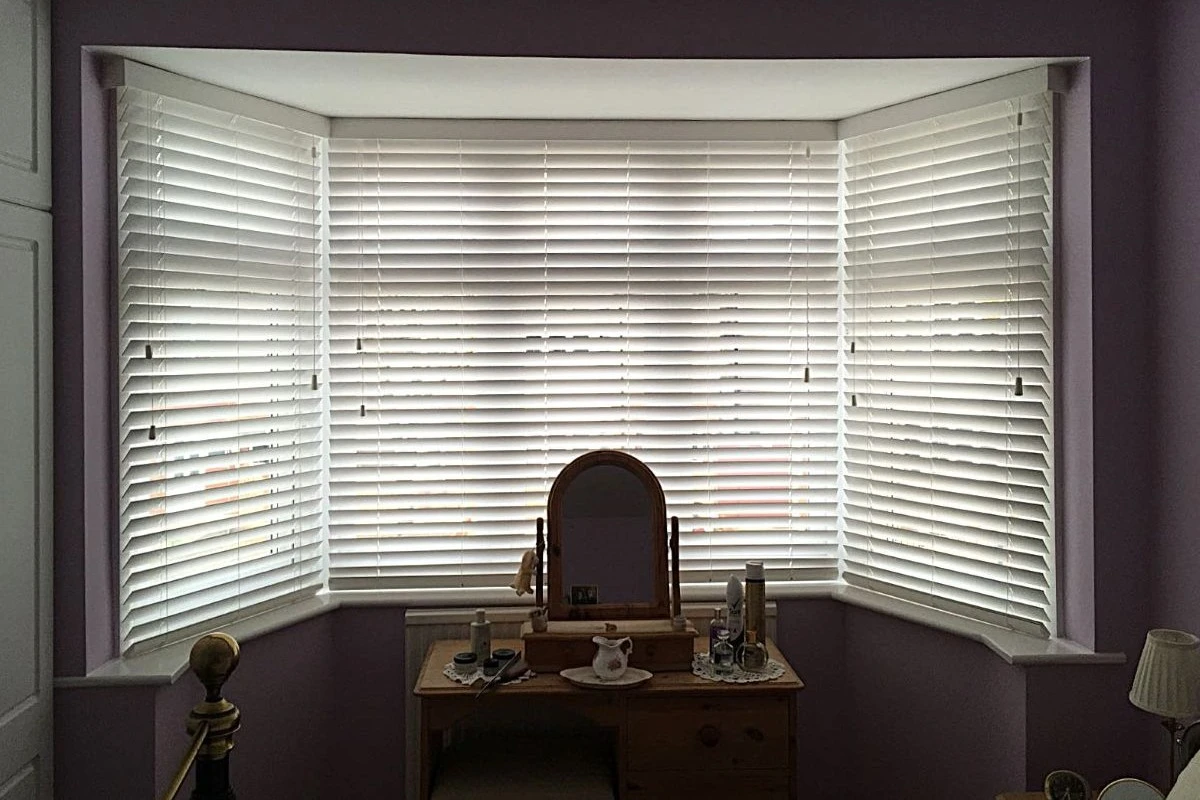 White Venetian Blinds in Bedroom Bay Window White faux wood Venetian blinds fitted inside a bay window in a bedroom.