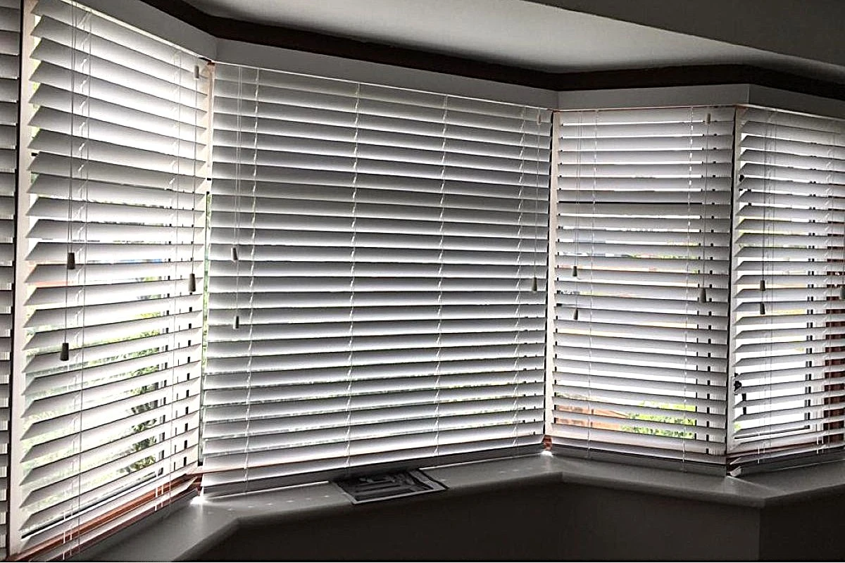 White faux wood venetian blinds in a bay window, Serene Fine Grain finish, providing privacy and adjustable light control.