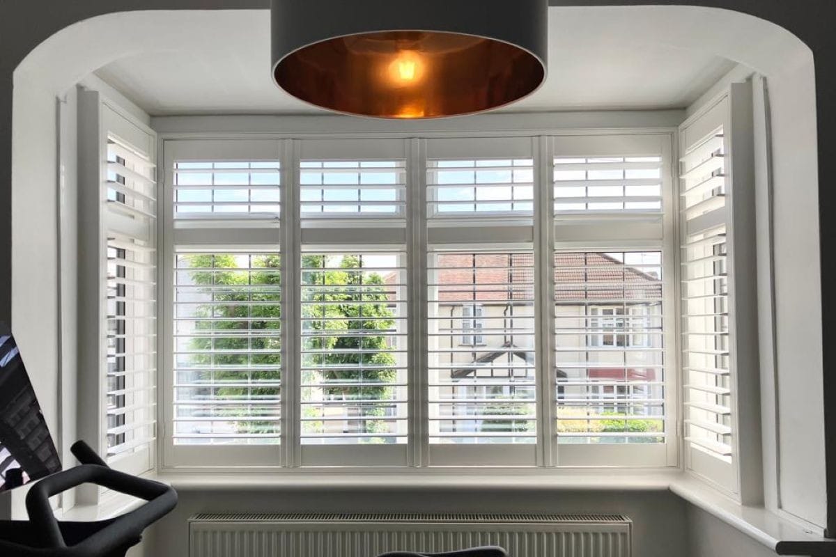 White plantation shutters providing adjustable light control in a bay window home office