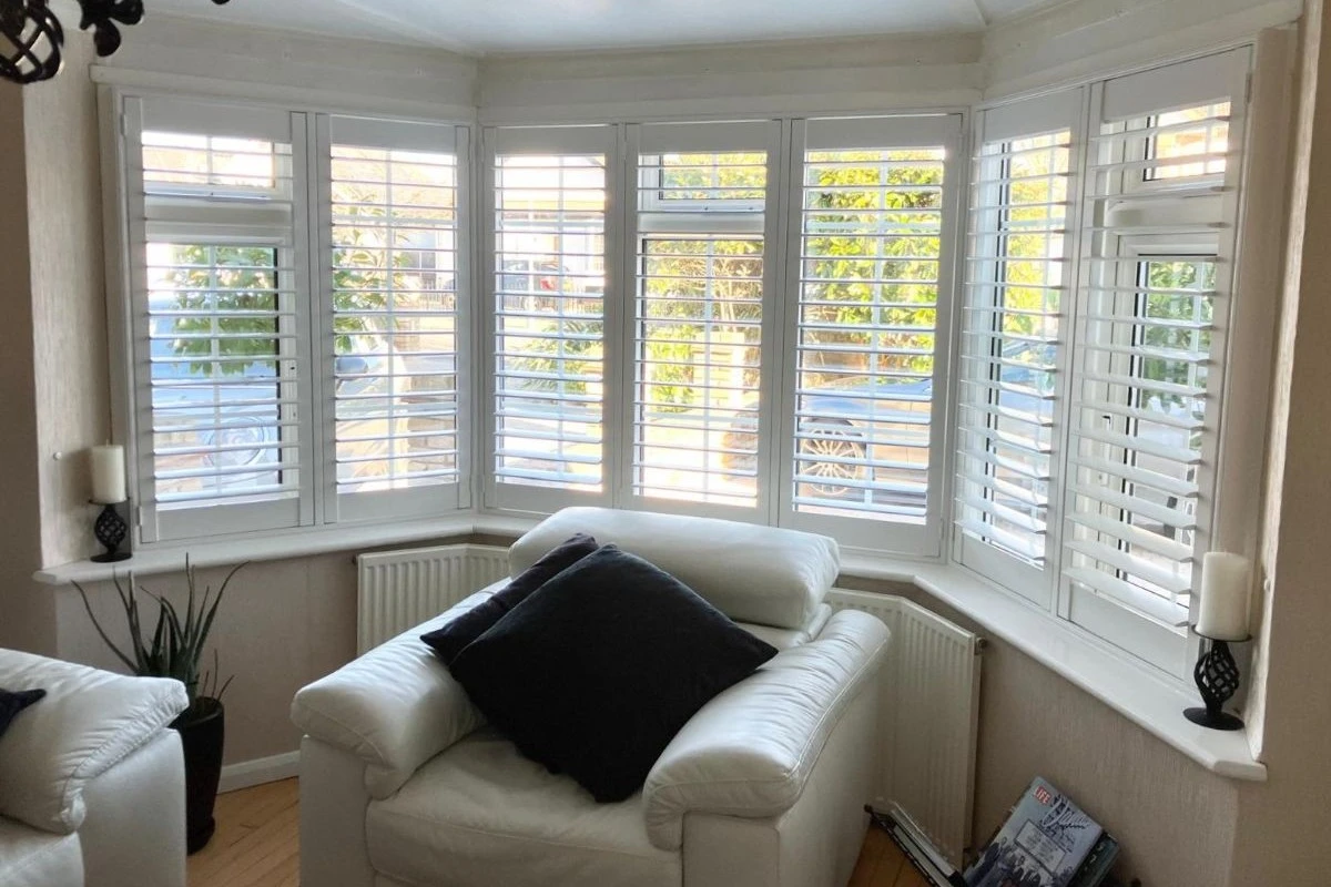 White plantation shutters fitted to a living room bay window providing light control and privacy
