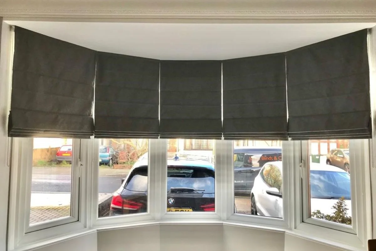 Charcoal Roman blinds fitted neatly within a bay window, following the shape of the bay for a tailored finish