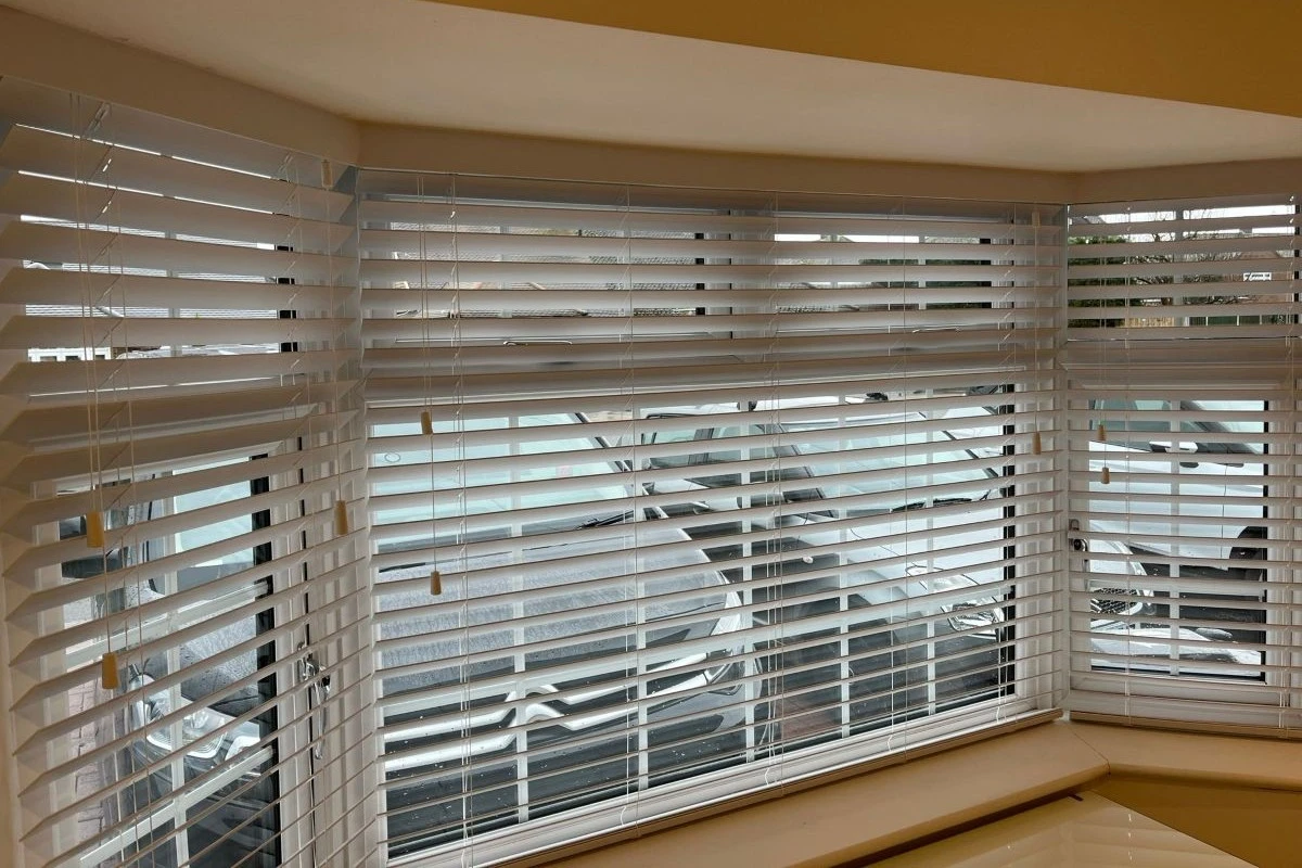 Faux wood Venetian blinds installed across a splay bay window, offering adjustable light control and privacy