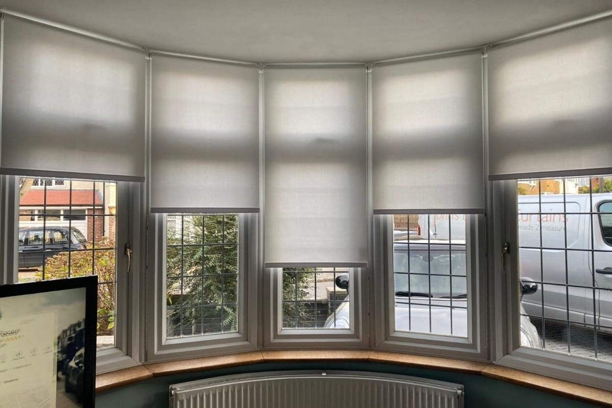 Grey roller blinds fitted neatly across a bay window, providing light control and a clean, modern finish