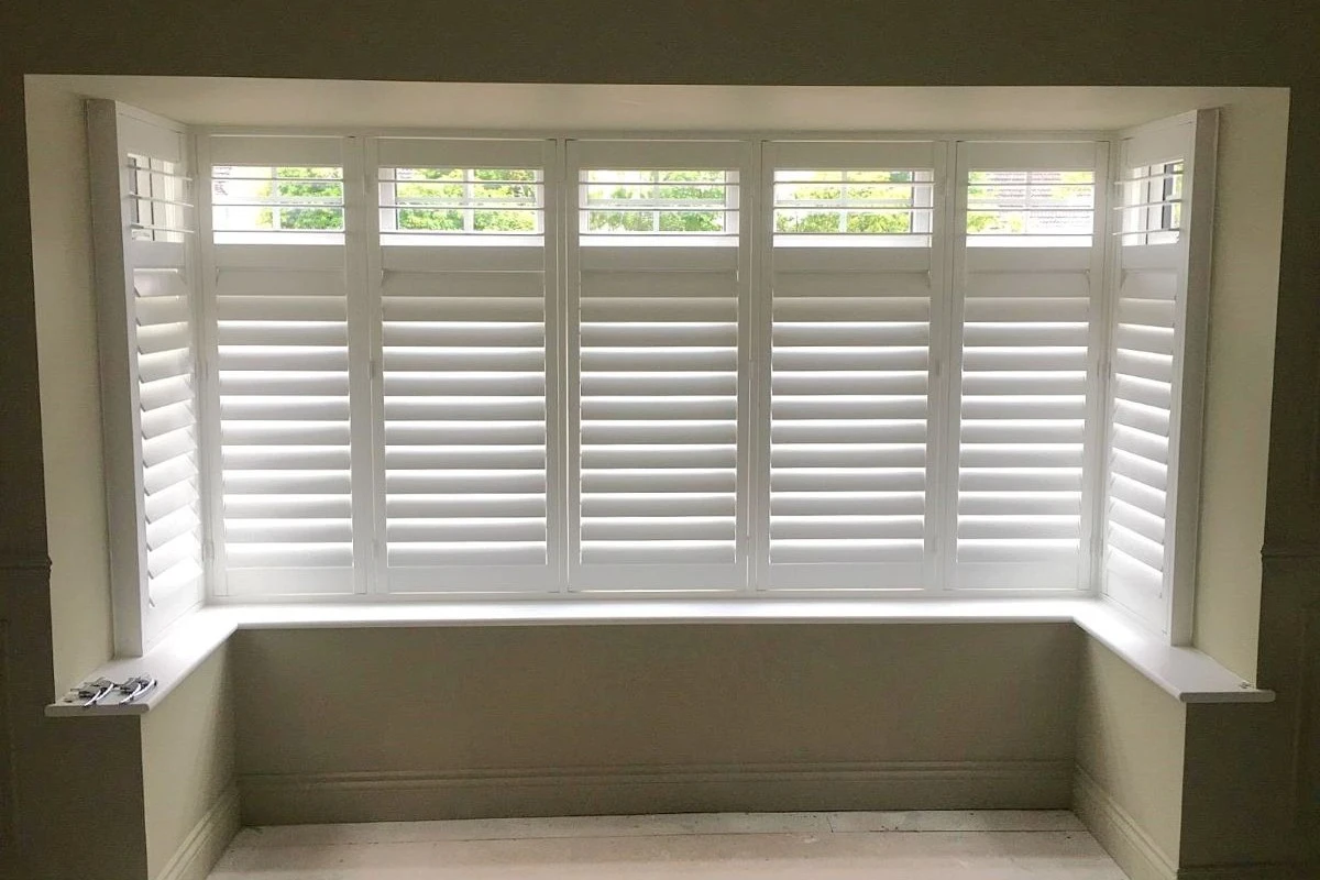 White plantation shutters fitted to a bay window with open top light panels for natural light