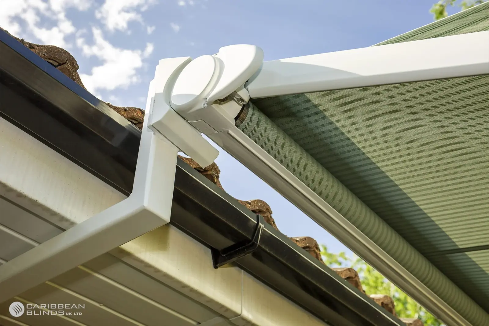 Close-up of a white Anguilla retractable patio awning arm and bracket mounted to a house roofline with green striped fabric extended.