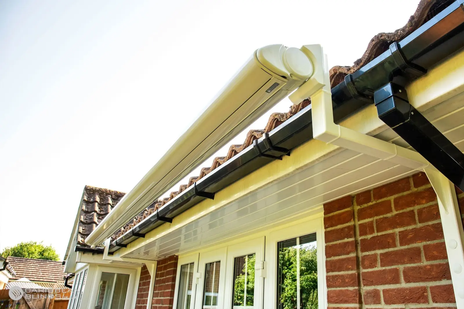 White Anguilla retractable patio awning in closed cassette position mounted above French doors on a brick house.