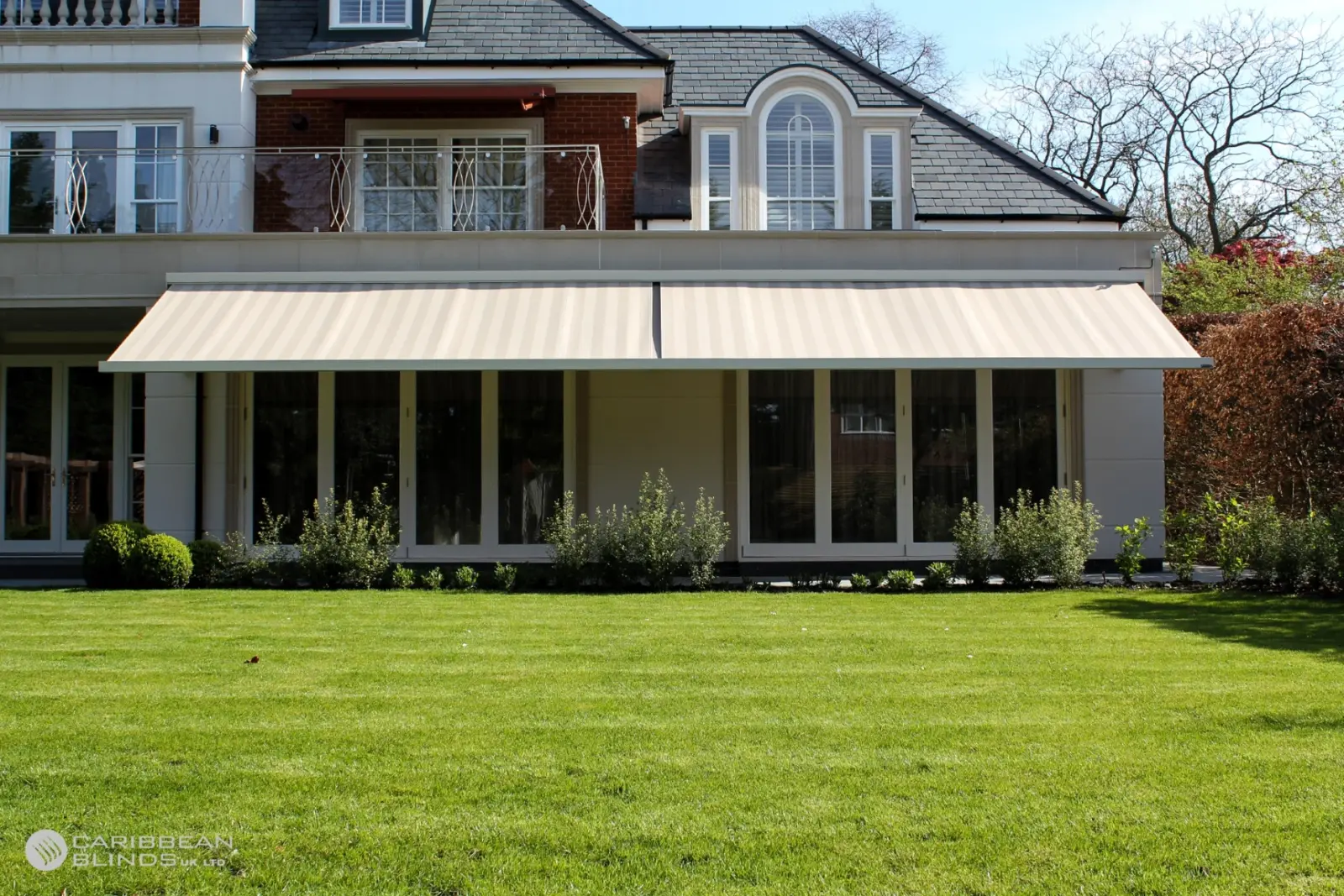Close-up of a white Anguilla retractable patio awning arm and bracket mounted to a house roofline with green striped fabric extended.