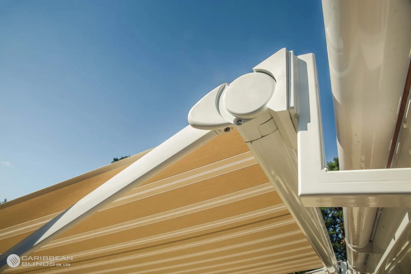 Close-up of a white Anguilla retractable patio awning arm and bracket mounted to a house roofline with green striped fabric extended.
