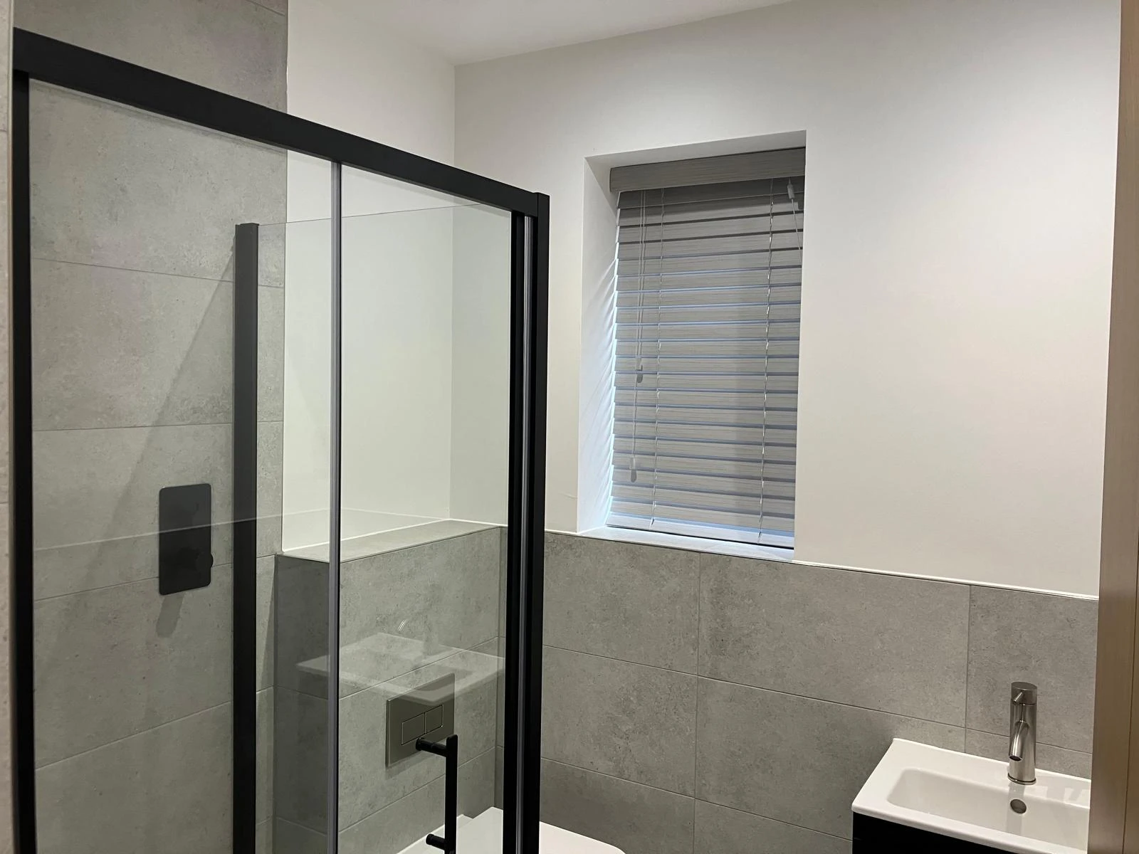 Grey faux wood Venetian blind fitted in a modern bathroom window, ideal for moisture-resistant performance.