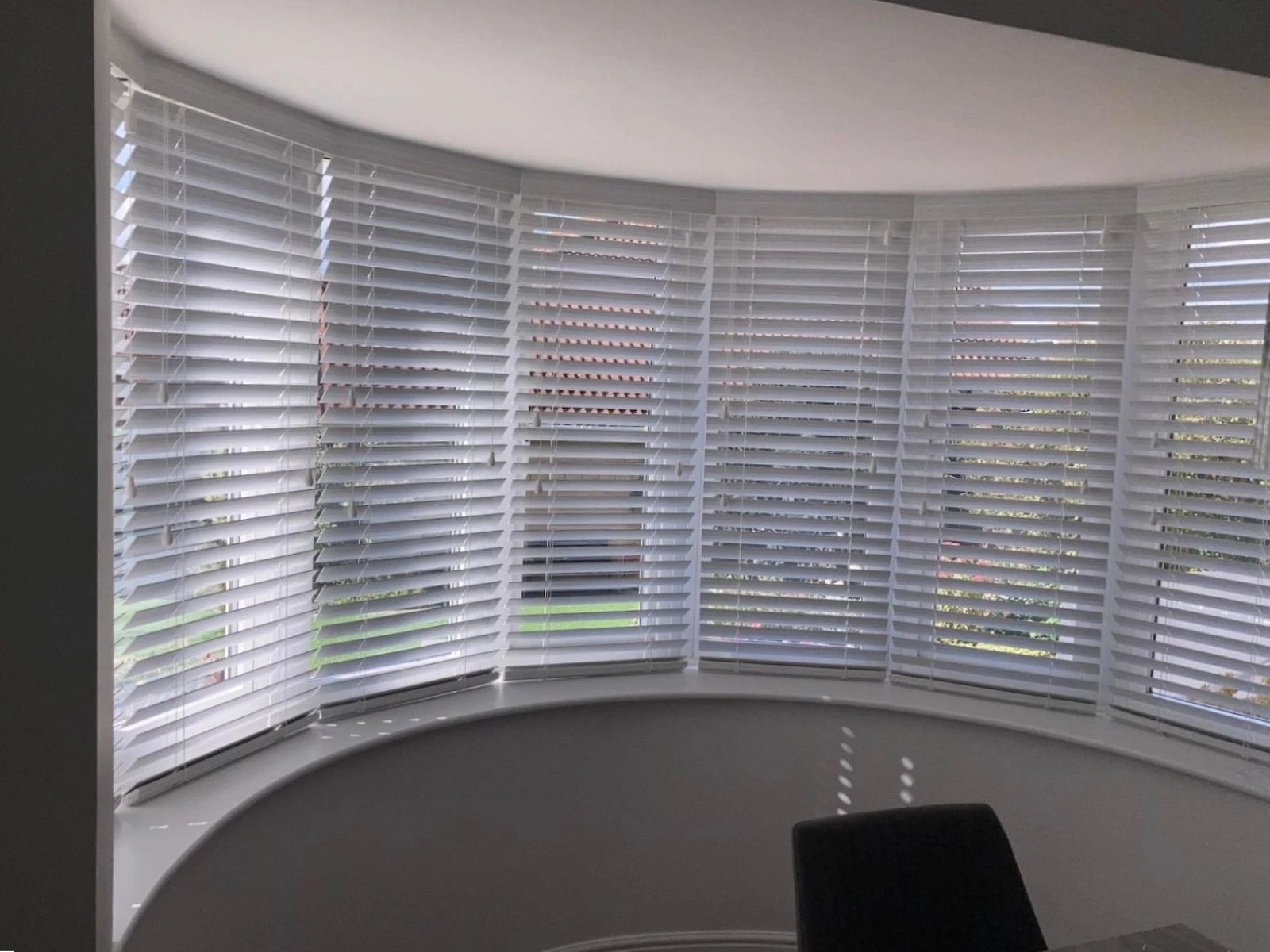 White Venetian blinds fitted across a curved bay window, providing privacy and adjustable light control.
