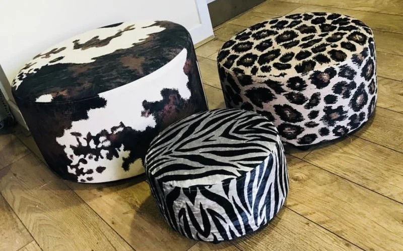 Set of upholstered footstools in zebra, leopard and cow print fabrics on wooden flooring
