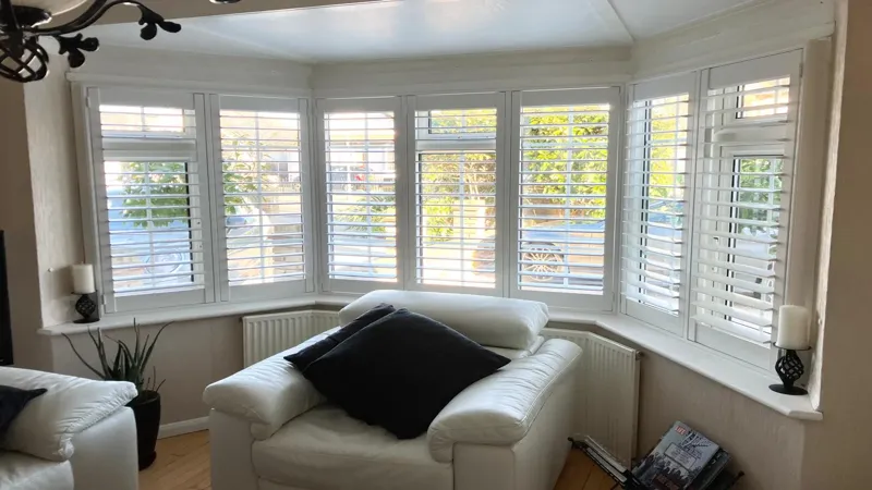 Bay Window Plantation Shutters Installed in Essex Living Room White plantation shutters fitted to a bay window in a bright Essex living room with armchair seating