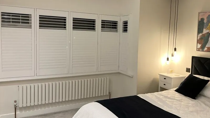 Full Height Plantation Shutters in Essex Bedroom Full height white plantation shutters fitted to a bedroom window in an Essex home with bedside lighting