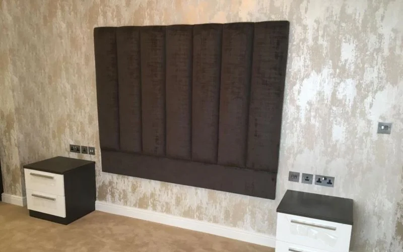 Custom brown upholstered headboard fitted to a bedroom wall with bedside units