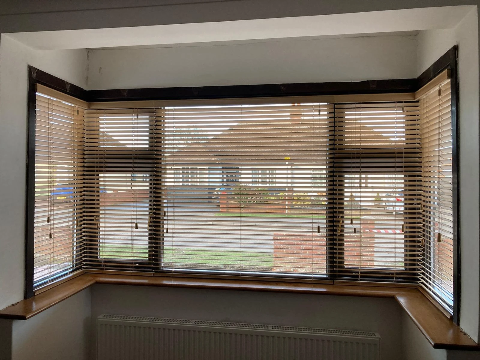 Light wood Venetian blinds installed in a three-sided bay window with matching wooden sill.