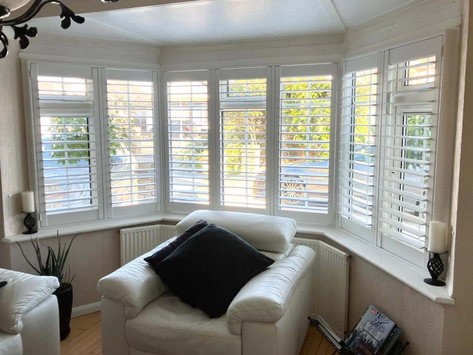White plantation shutters fitted to a bay window in a living room, providing light control and privacy with a precise made-to-measure fit