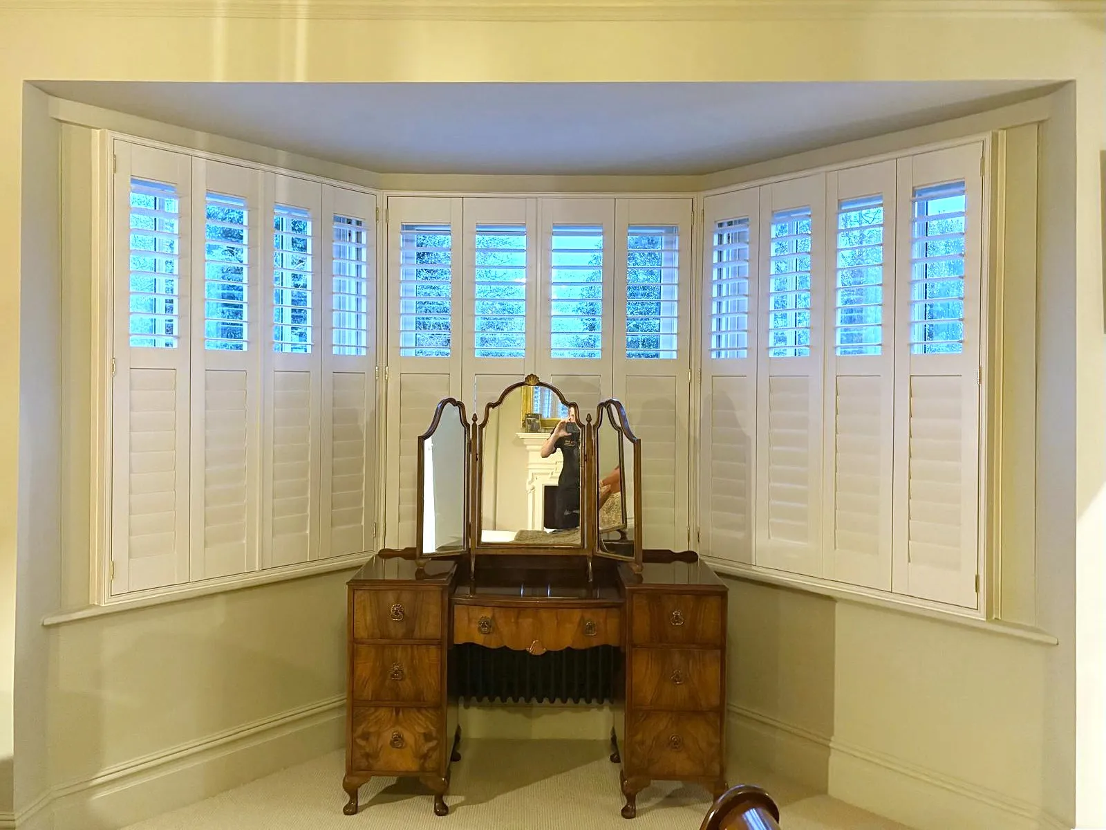 Full height plantation shutters fitted to a bay window in a bedroom, designed to follow each angle for a precise made-to-measure fit