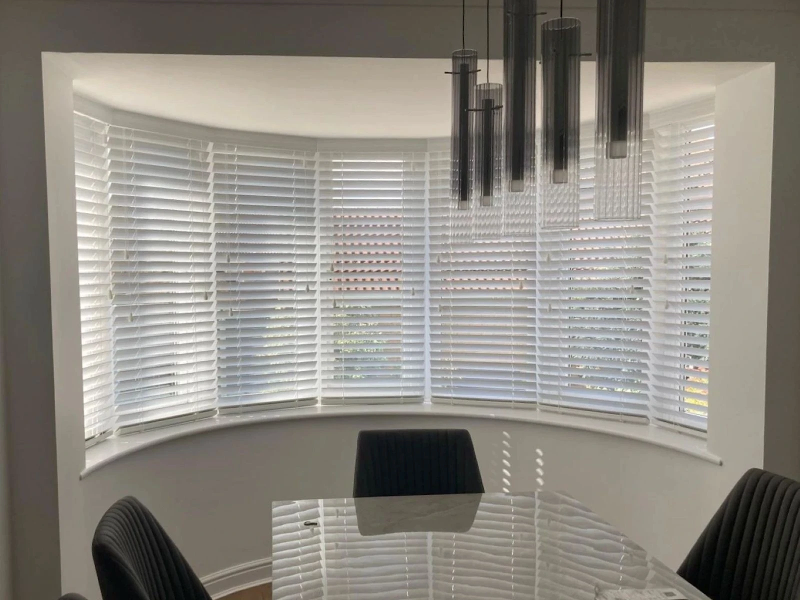 White Venetian Blinds fitted within a curved bay window in a modern dining room interior.