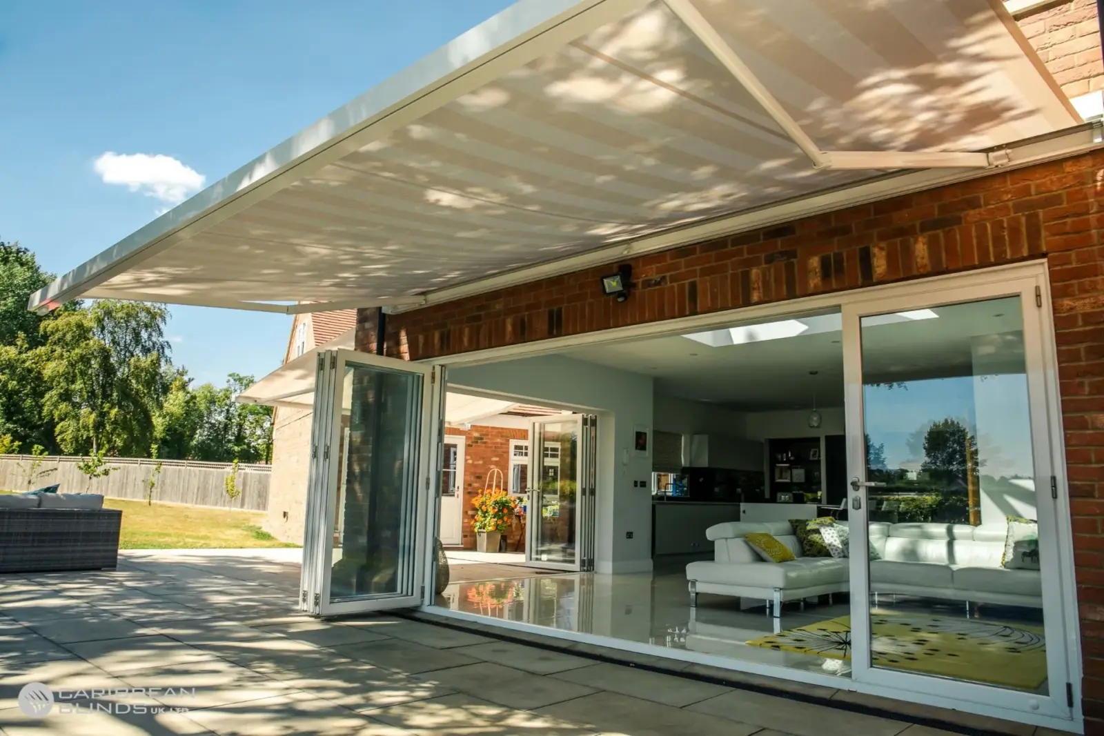 Retractable patio awning providing shade over patio with open bifold doors in Essex home