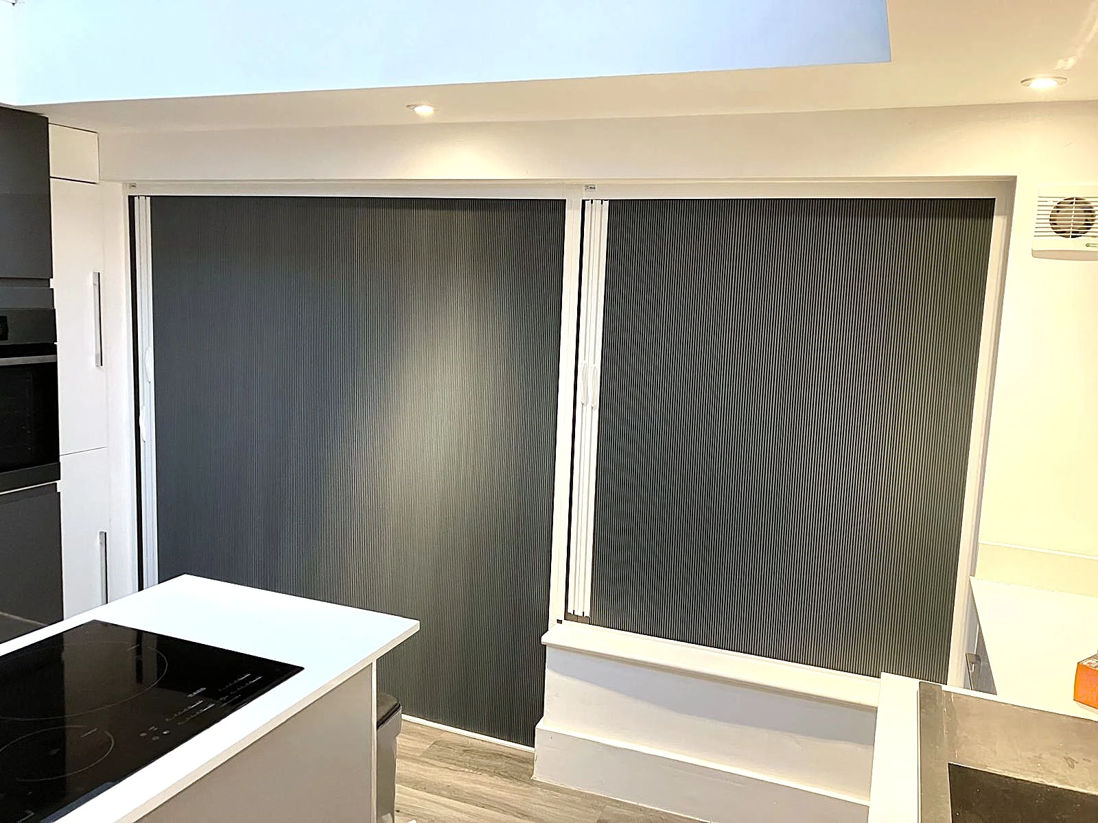 Blind Screen blackout systems installed across large windows within an open plan kitchen and living space to improve room darkening and reduce glare.