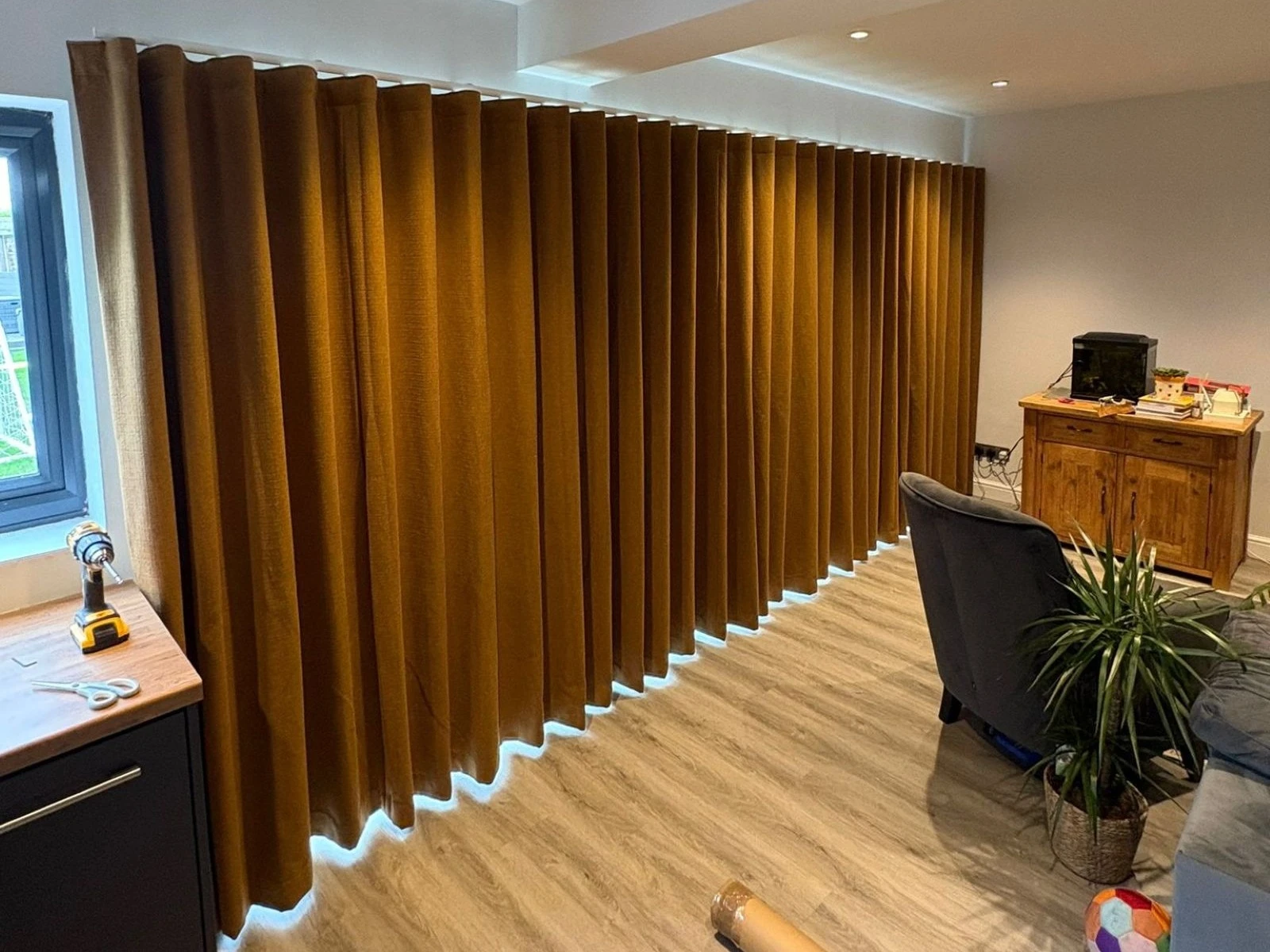 Brown wave curtains installed in a modern open-plan living space with full-height glazing and wood flooring.