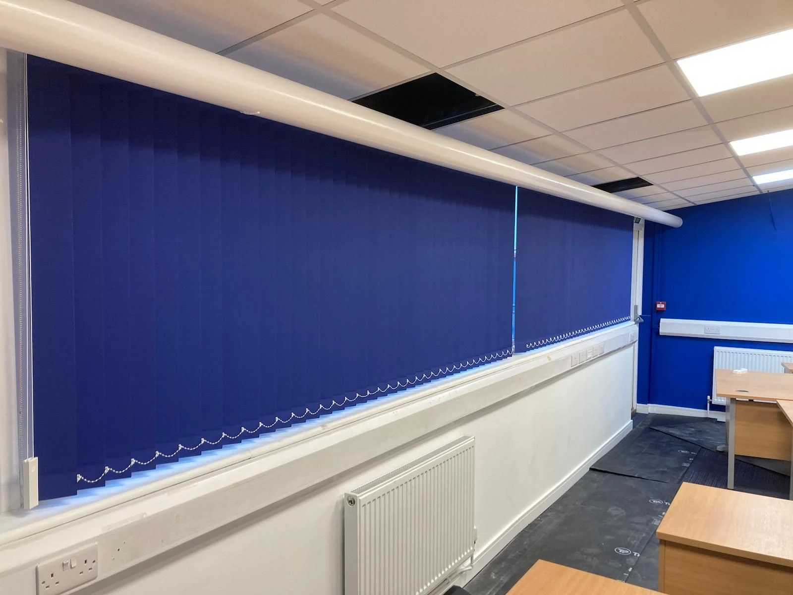 Blue commercial vertical blinds fitted within an office in Essex, providing glare control, privacy and light management across a large window.