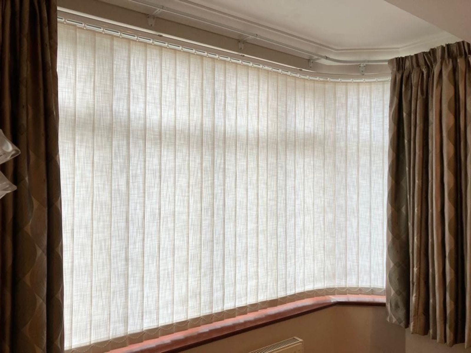 Light filtering vertical blinds installed within a hockey stick bay window in an Essex home, offering adjustable privacy and light control across the angled window layout.