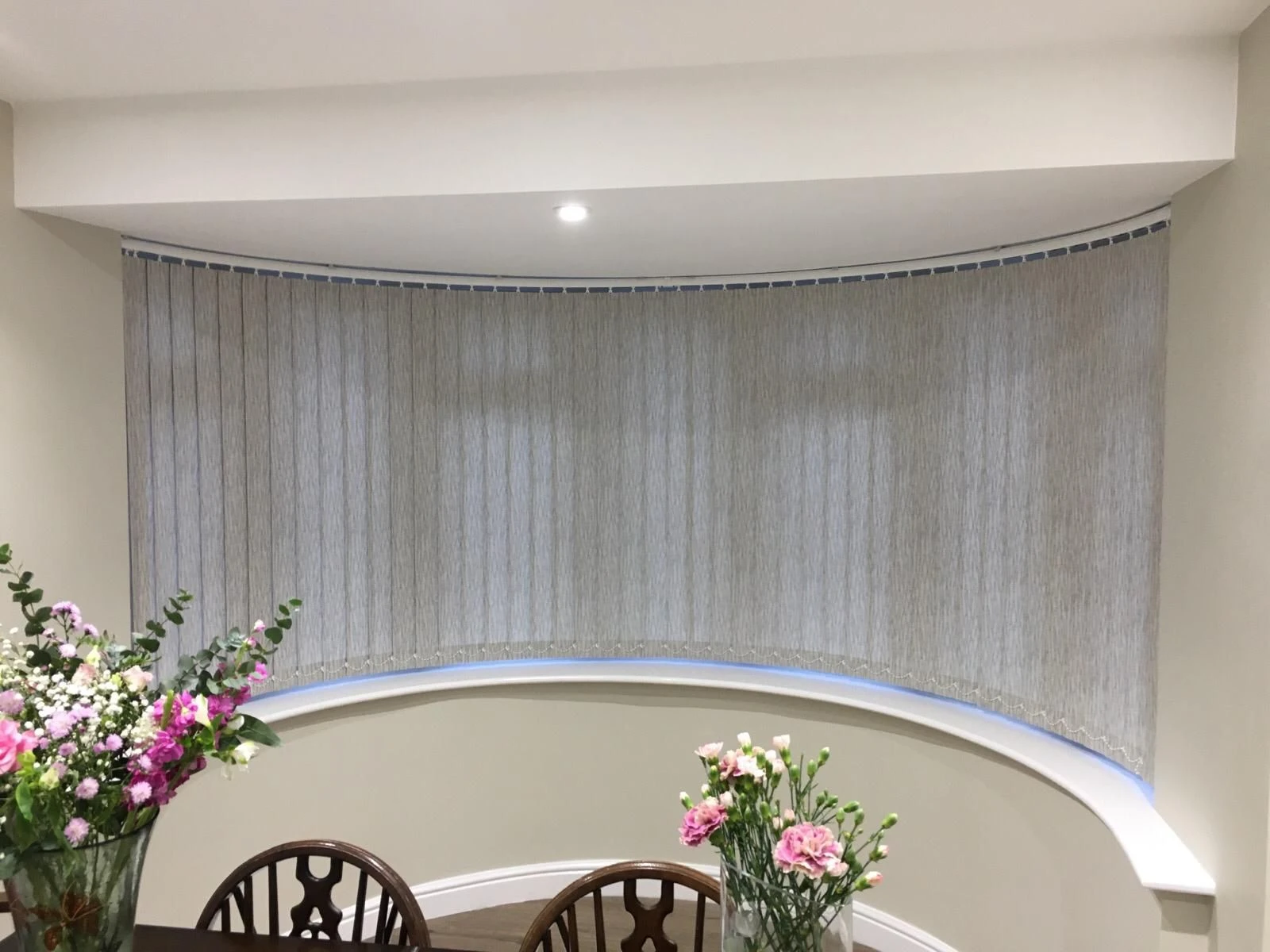 Light grey curved vertical blinds fitted to a curved bay window in an Essex home, offering privacy and light control with a custom curved track system.