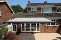 Grey motorised retractable patio awning fully extended over a rear garden patio at a brick family home in Essex.