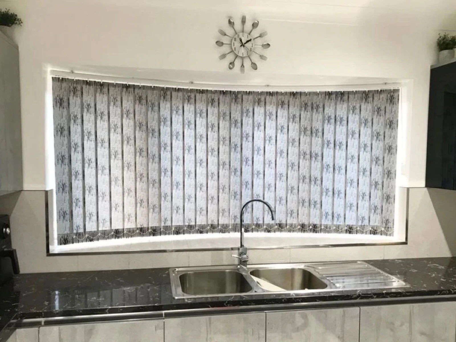 Patterned curved vertical blinds installed within a curved kitchen window in an Essex home, providing adjustable privacy and light control across shaped glazing.