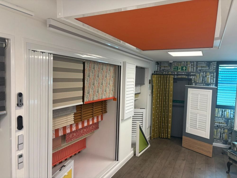 Orange roof lantern blind displayed above window blind, curtain and plantation shutter displays inside John’s Blinds & Curtains’ Wickford showroom.